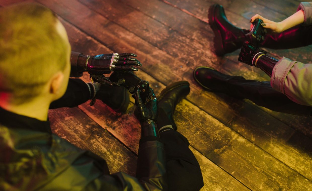 Two people with prosthetic hands playing video games on a wooden floor.