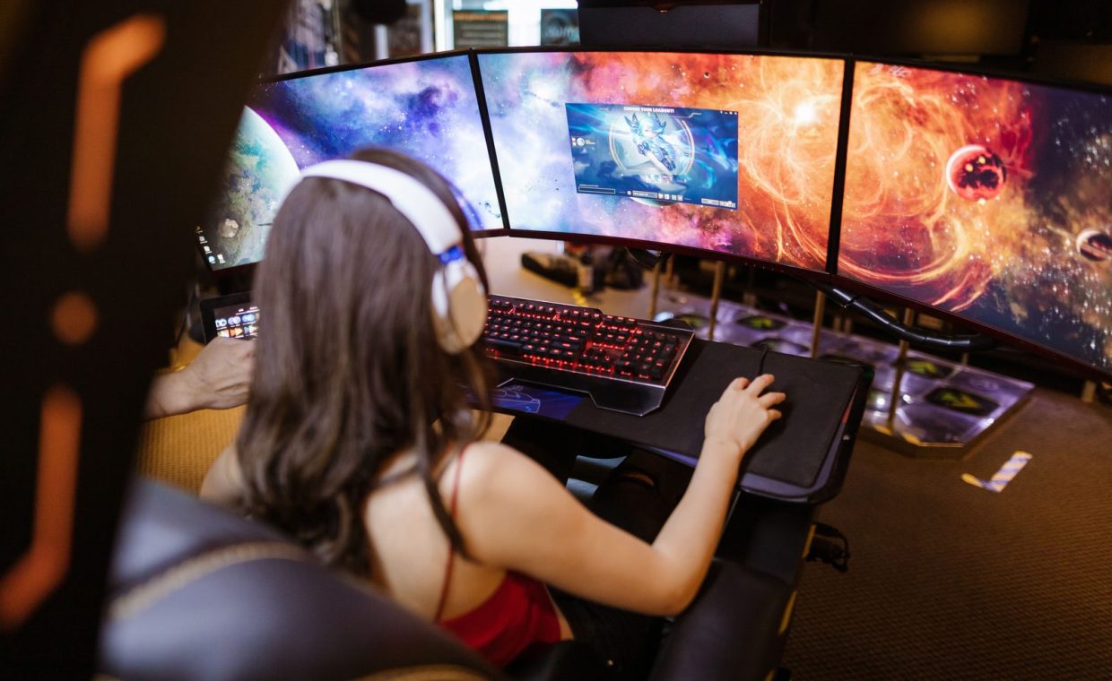 Woman with headphones playing on a multi-screen gaming setup featuring vibrant space imagery.