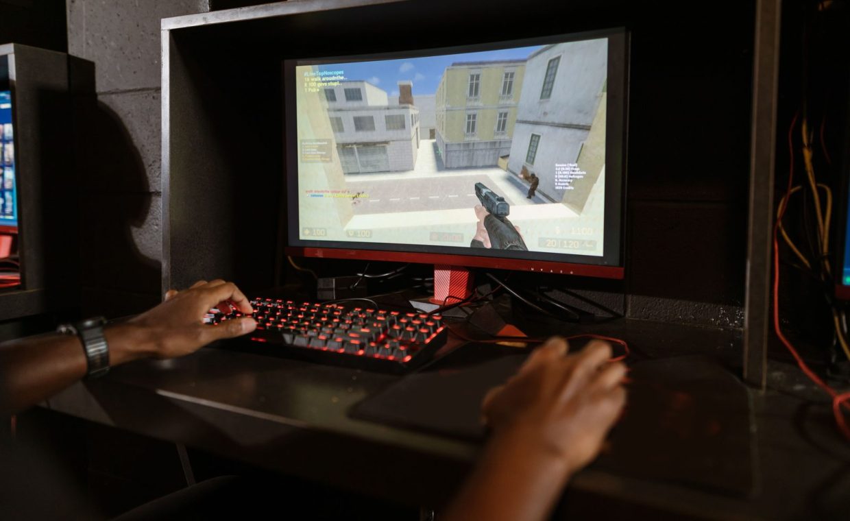 Person engaging in a shooting video game on a high-performance setup with mechanical keyboard.