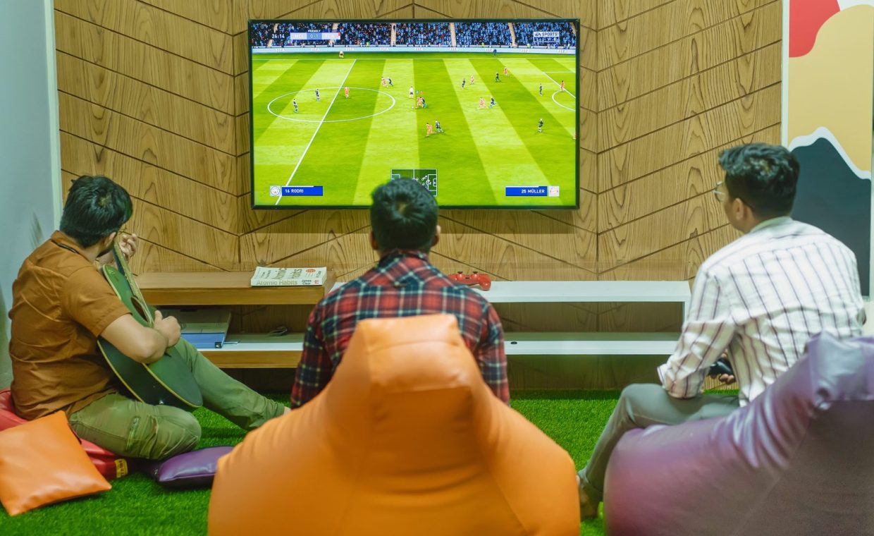 Three friends relaxing and playing a soccer video game indoors on a comfortable game night.