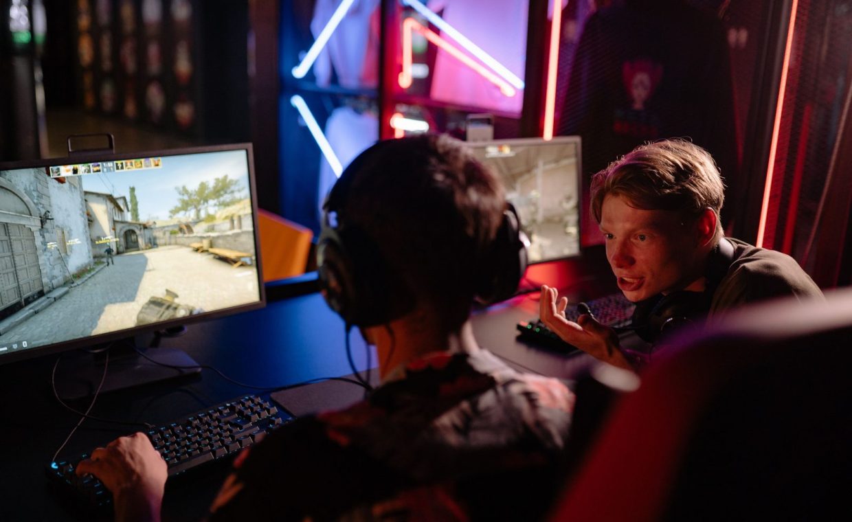 Two gamers engaged in a heated video game session surrounded by neon lights and computer screens.