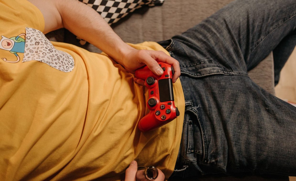 Person holding a red game controller while relaxing on a couch in comfortable clothes.