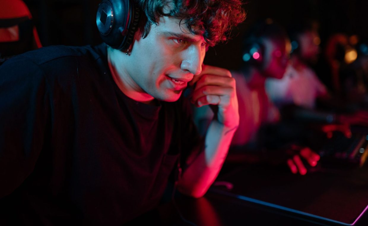 Close-up of a focused gamer wearing a headset in a dimly lit environment, immersed in an intense gaming session.