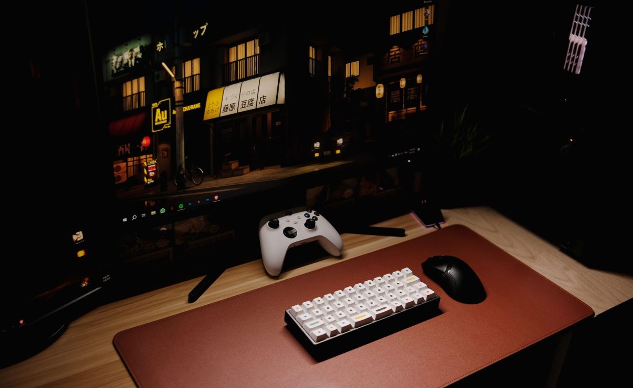 Close-up of a gaming desk setup featuring a keyboard, controller, and monitor at night.