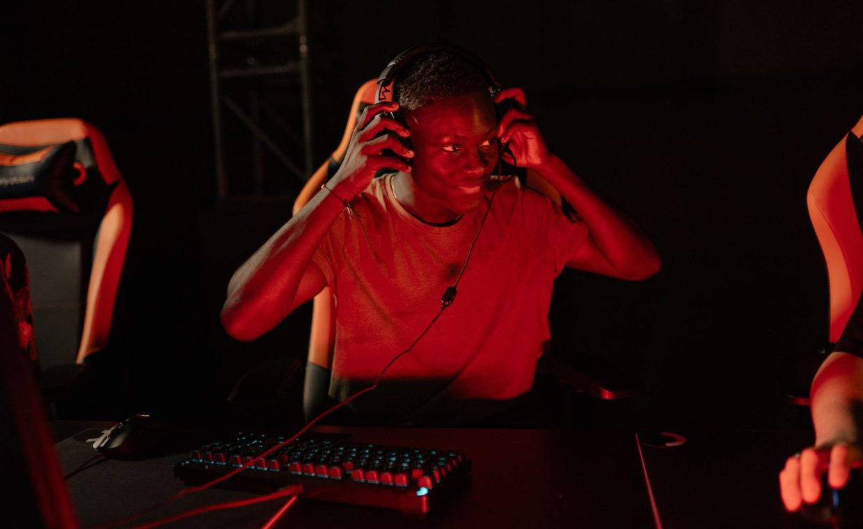 A young man enthusiastically gaming in a dimly lit room with headphones on.