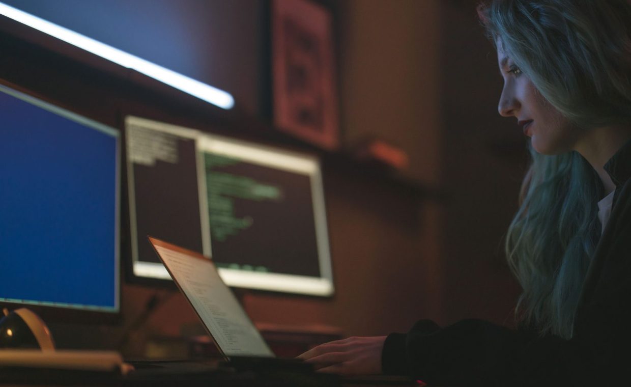 Woman working on cybersecurity programming with laptops and multiple screens