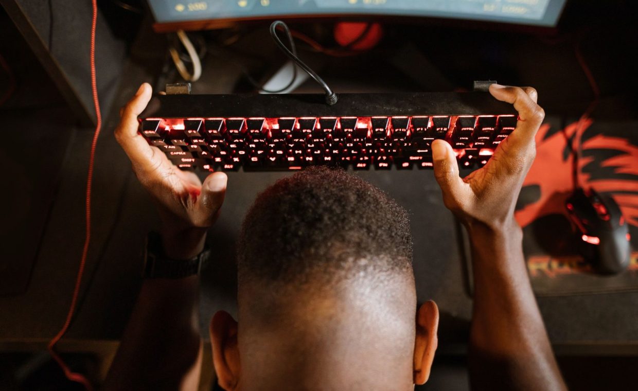Gamer expresses frustration with video game by holding up keyboard. Overhead shot of gaming setup.