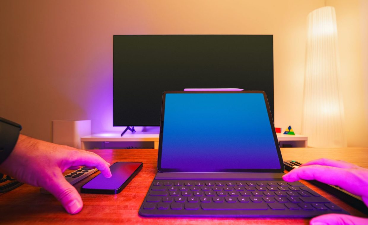 A vibrant workspace featuring a laptop, tablet, and TV with colorful lighting.