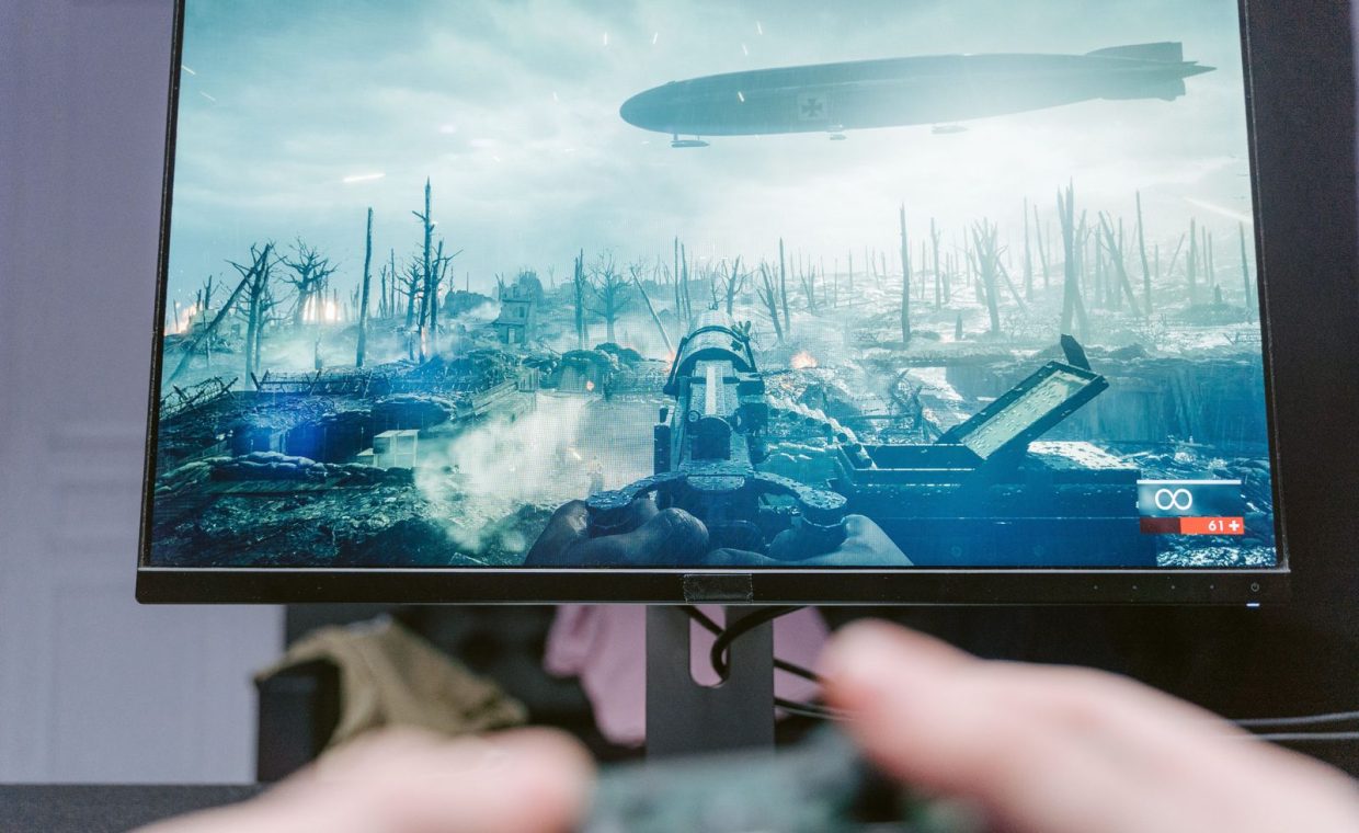 A person playing a video game on a high-resolution monitor, showcasing a war-themed landscape.
