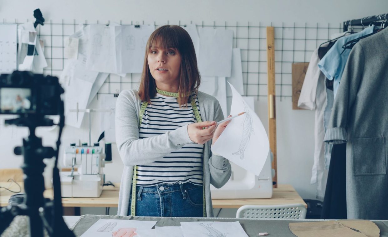 Female fashion designer explaining her sketches on camera in a studio setup.