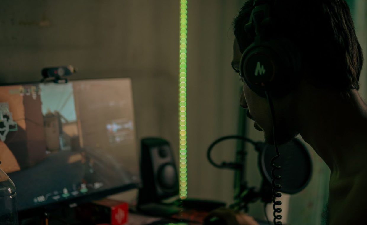Focused gamer with headset playing a video game on a desktop computer indoors.