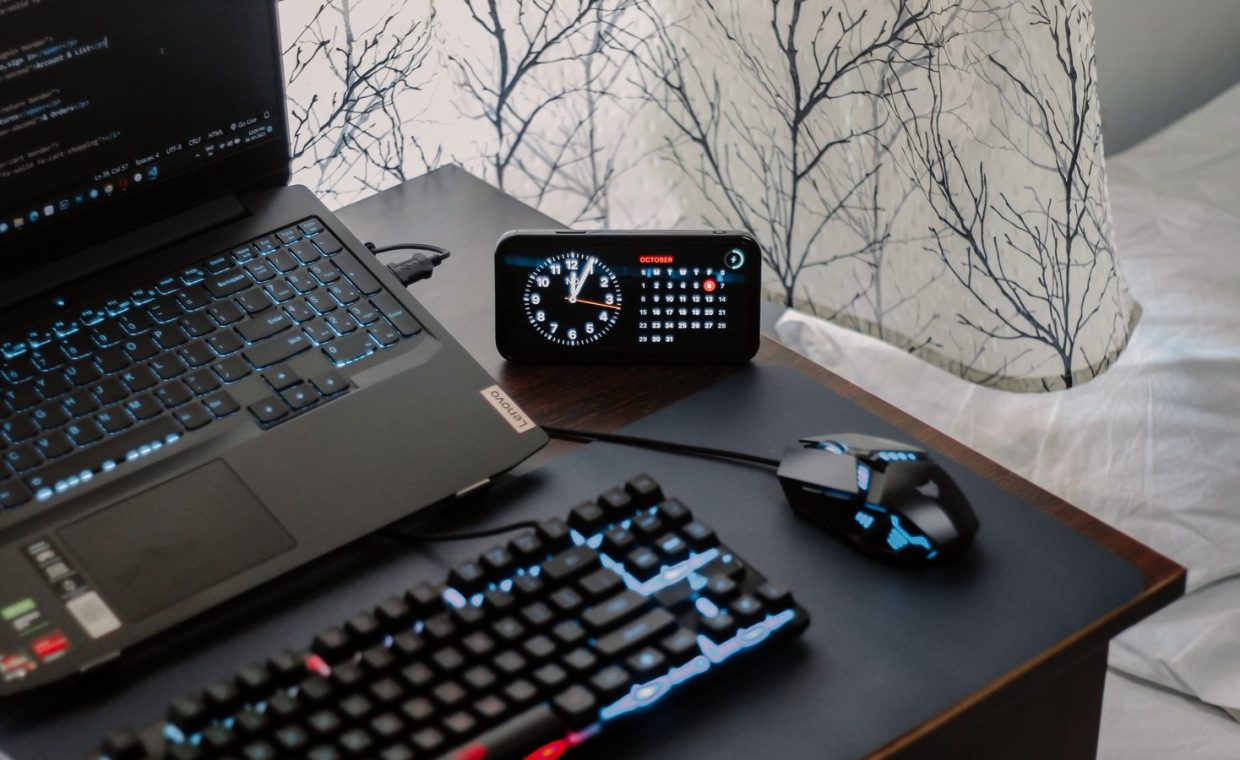 A modern workspace featuring a laptop, digital clock, gaming mouse, and keyboard, ideal for work and tech enthusiasts.
