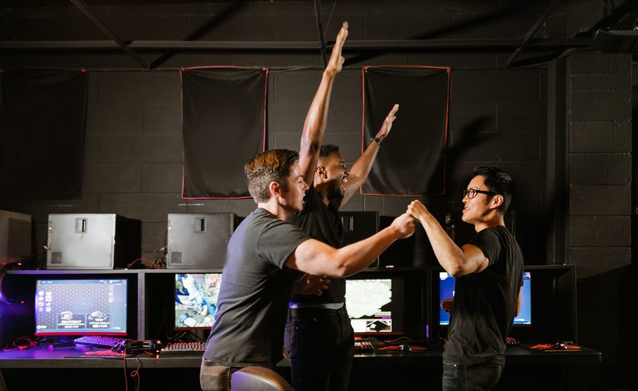 Three excited gamers celebrating their victory in an esports gaming arena, showing teamwork and joy.