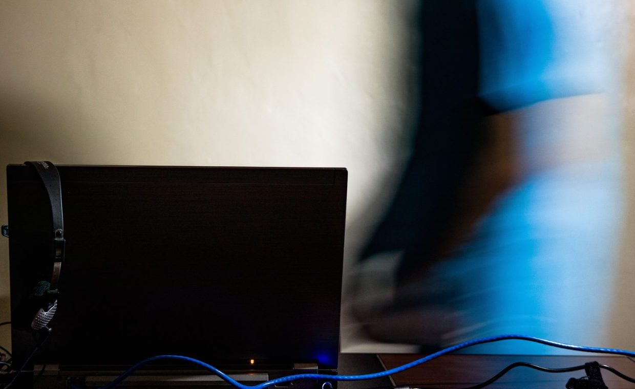 Long exposure of anonymous male in blue t shirt walking toward black computer in light room