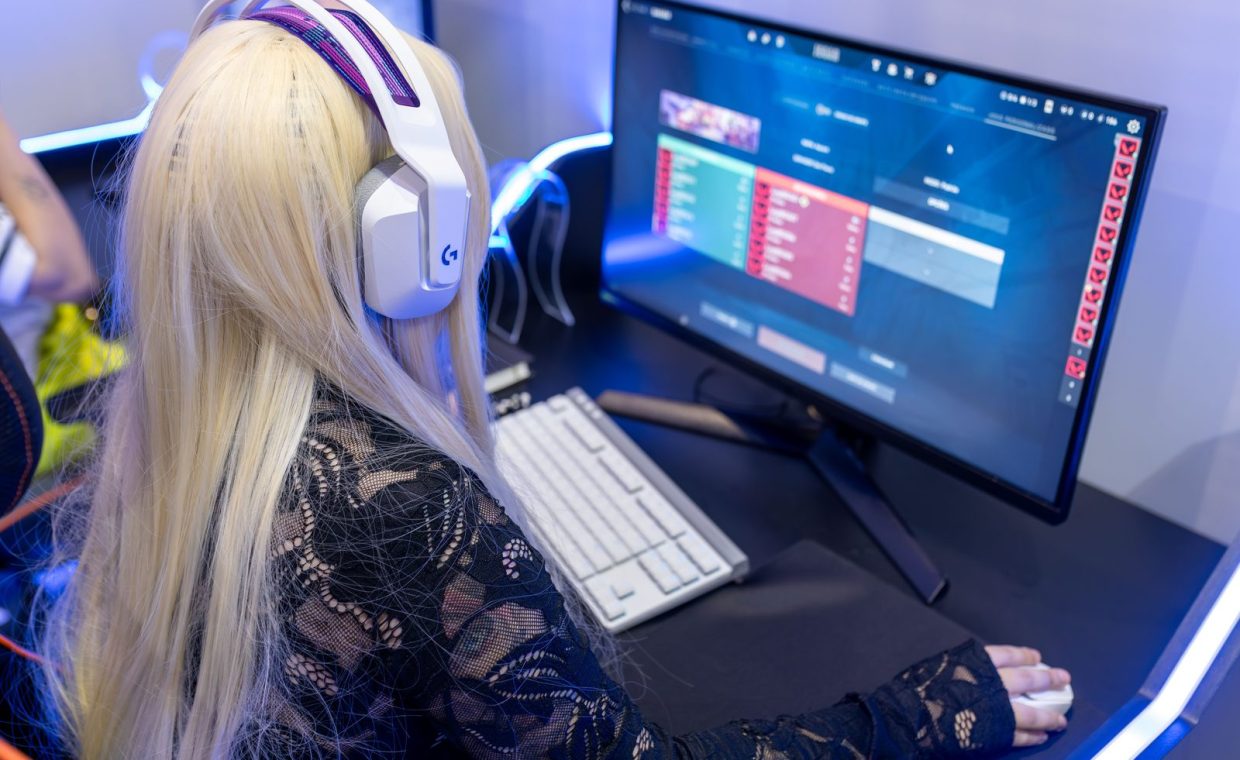 Young woman gaming at a PC high-tech setup, wearing headphones.