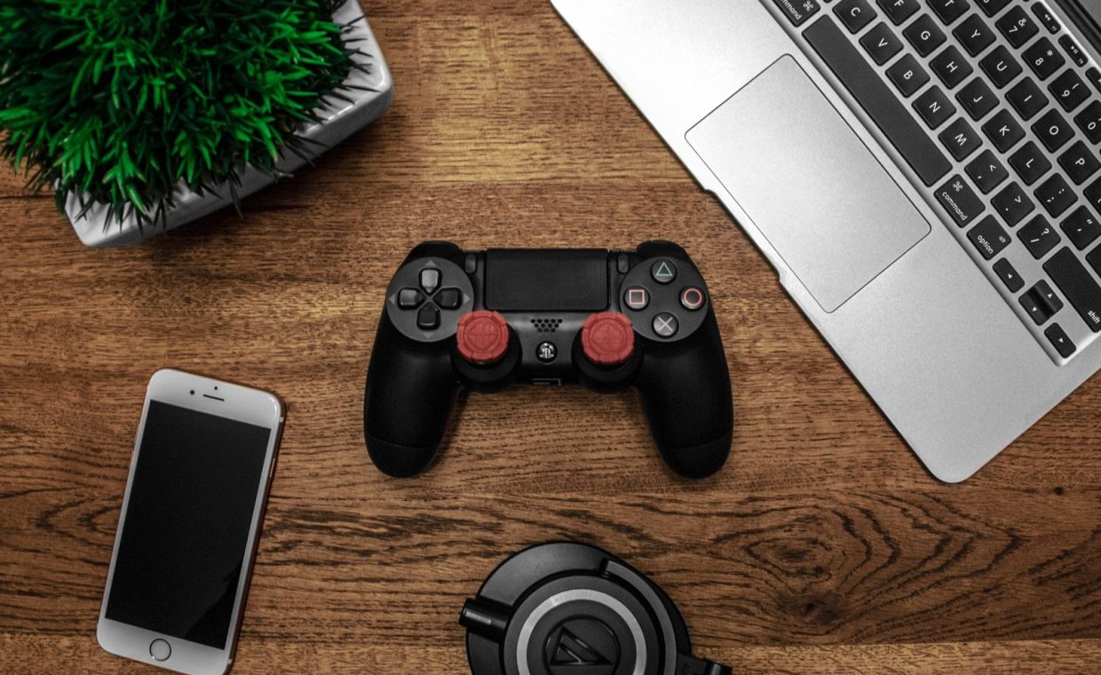 A flat lay photo showcasing a gaming console, laptop, smartphone, and headphones on a wooden tabletop.