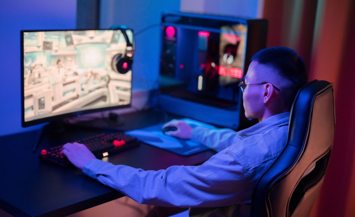 A young man intensely gaming on a computer at home, showcasing a modern gaming setup.