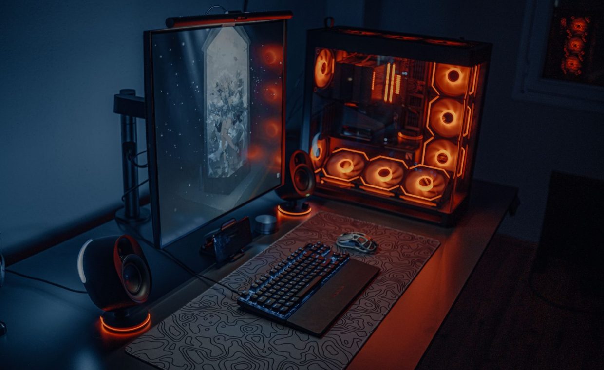 Sleek gaming desk setup featuring RGB lighting, large monitor, and gaming PC with glowing fans.