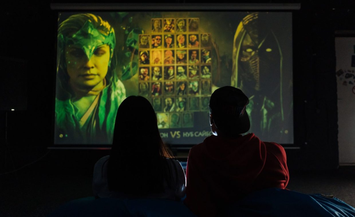 Two people sitting indoors gaming on a large projector screen, enjoying a video game session.