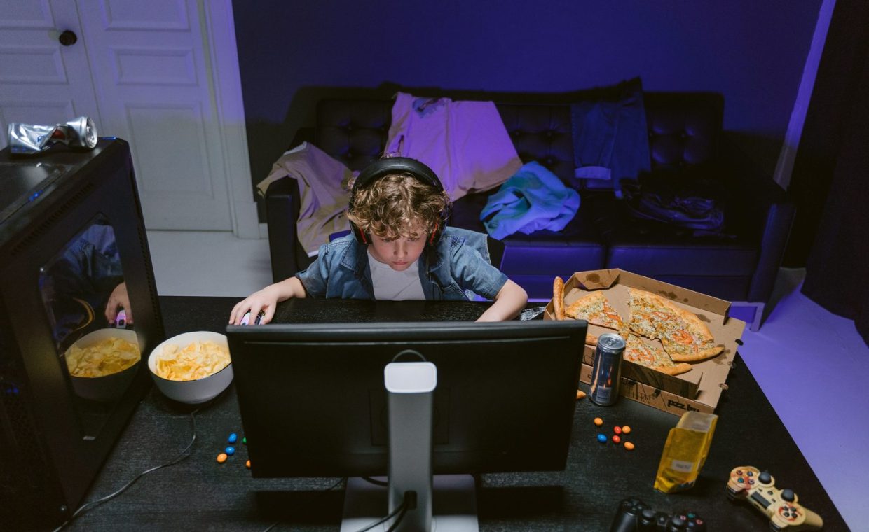 A young boy plays video games at home, surrounded by snacks, showcasing the gaming lifestyle.