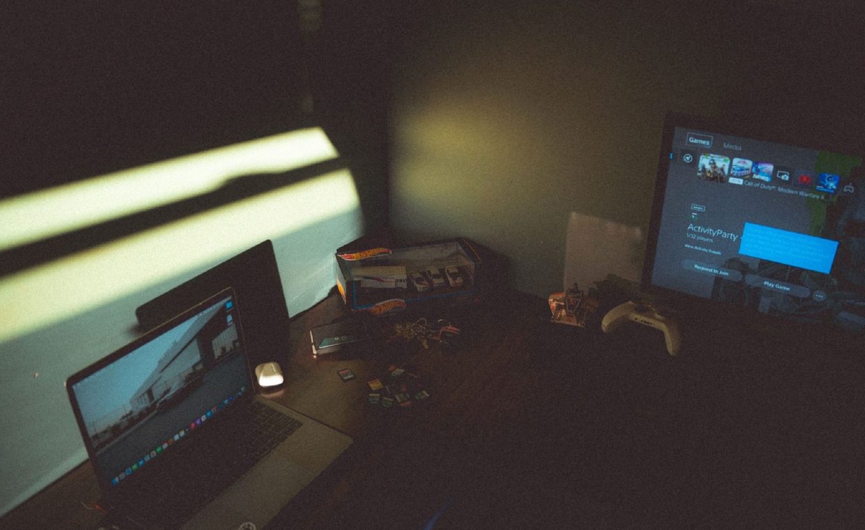 Dark room with a laptop and gaming console creating a moody tech atmosphere.