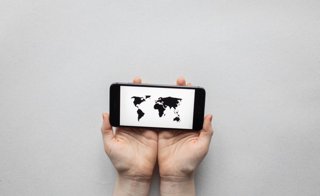Hands holding a smartphone displaying a world map on a white background.