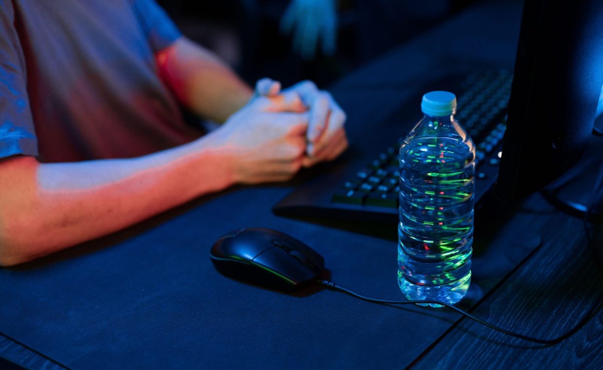 A close-up view of a gaming setup featuring a water bottle and computer mouse in a dimly lit environment.